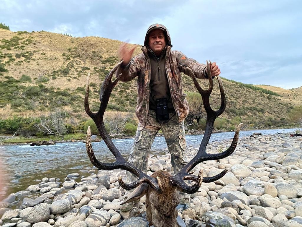 Cazador en río patagónico con cornamenta de ciervo mayor Red Stag
